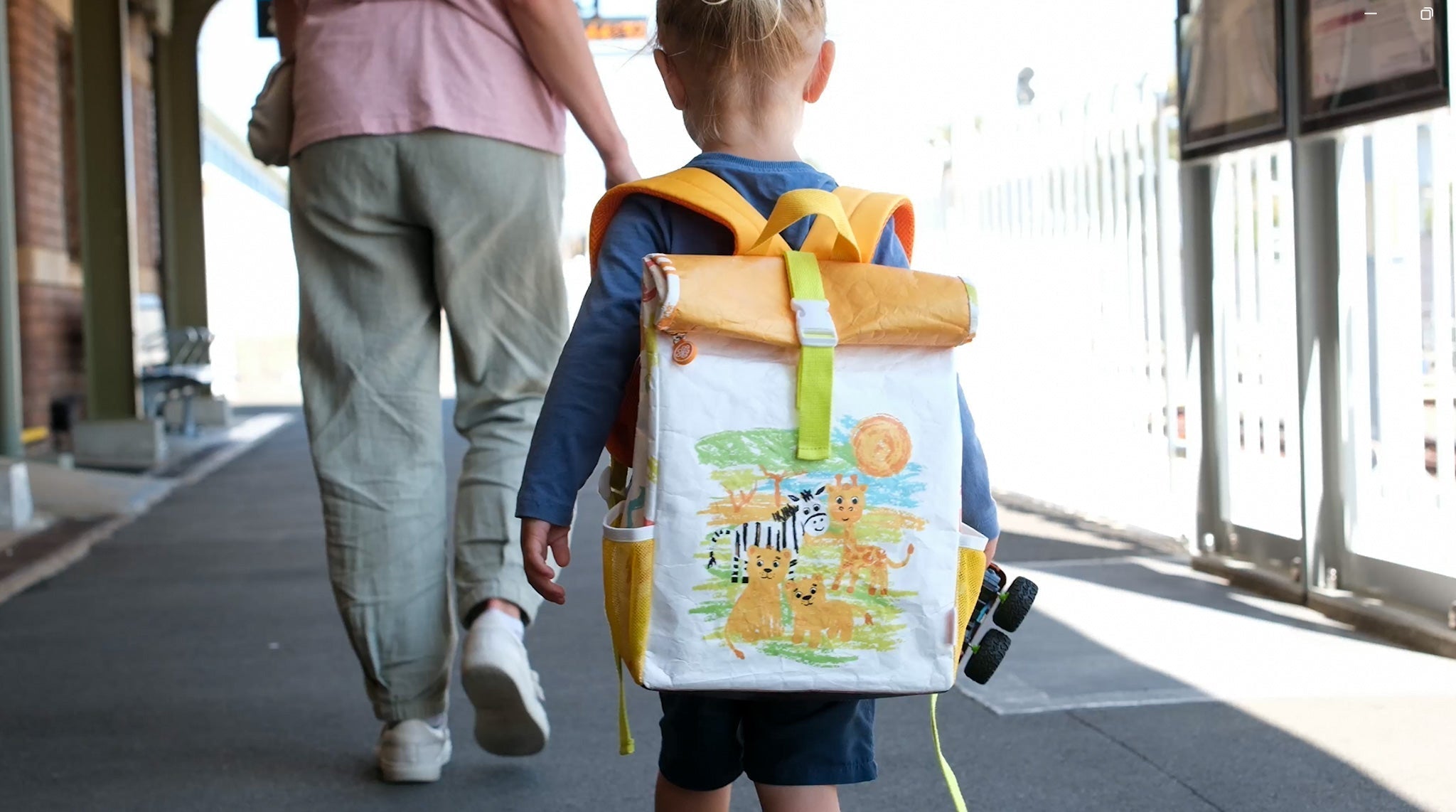 Toddler wearing a colourful Twisty Kids backpack while walking with an adult, highlighting family travel safety and kid-friendly travel accessories.