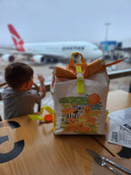 Children's backpack with animal illustrations on a table at an airport, with a Qantas airplane in the background.