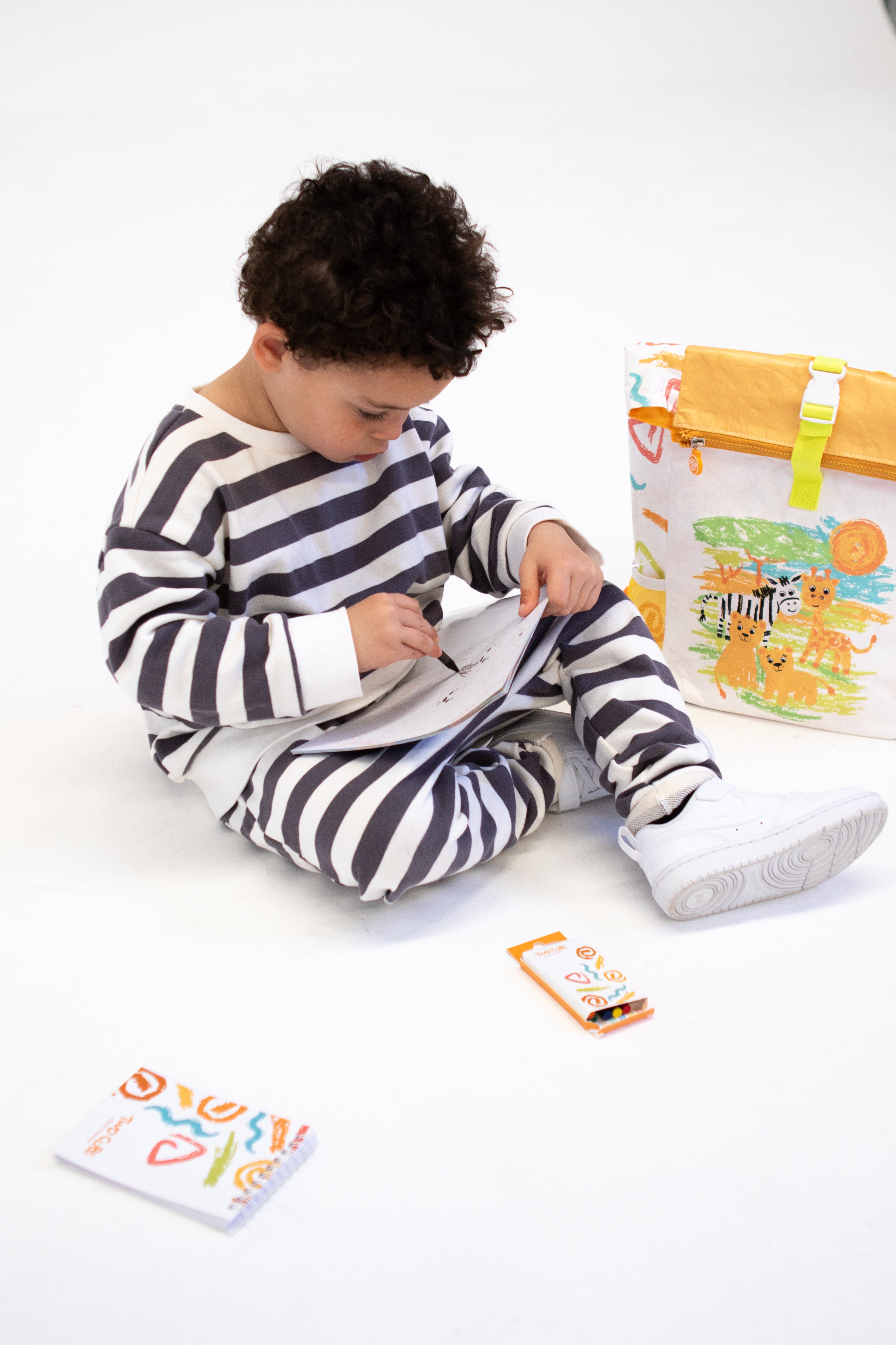 Child in striped pajamas sitting on a white floor and playing with travel activity pack that include in the Twisty Kids backpack