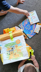 Children playing with travel pack, that includes colourful activity books, crayons, notebook and a preschool backpack on a carpeted floor