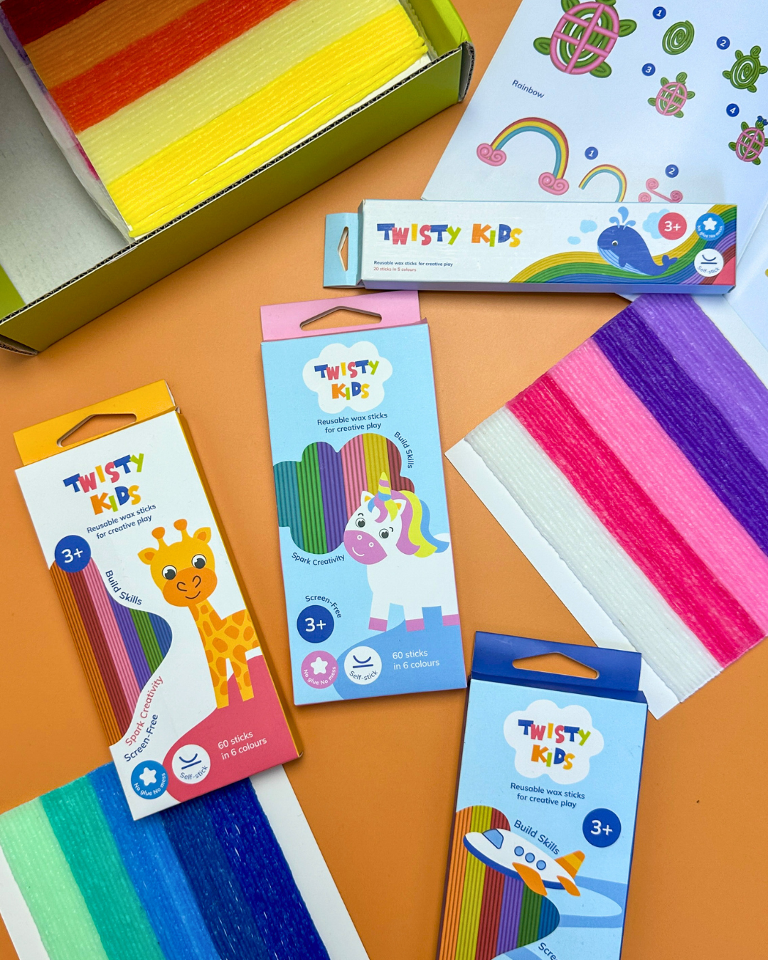 Twisty Kids wax stick packs, a folded box, and coloured strips arranged on an orange surface.